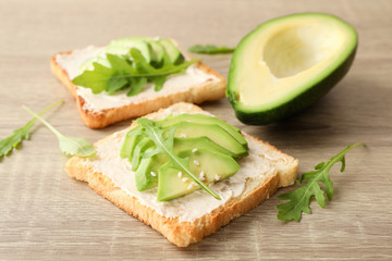 Toasts with butter, avocado, arugula and sesame on wooden background, close up