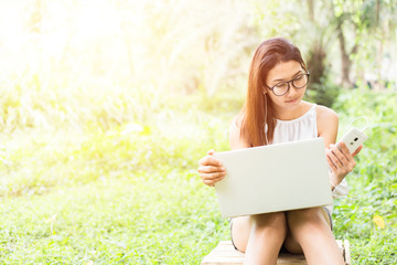 the women sitting on the wood box and working with notebook. She working in the park and color orange and green.