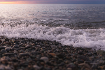 Sea sunset with pebble beach. The sun reflects on water, waves and stones creating a beautiful reflection. Beautiful sky and clouds
