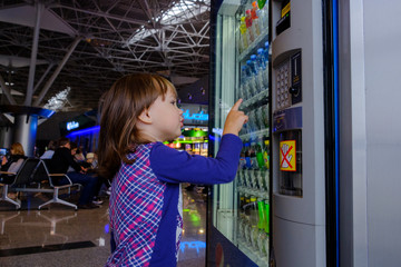 Moscow Vnukovo Airport 02082019: little child girl chooses a drink in the vending machine while waiting for boarding - obrazy, fototapety, plakaty