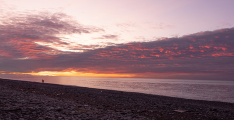 Obraz premium Sea sunset with pebble beach. The sun reflects on water, waves and stones creating a beautiful reflection. Beautiful sky and clouds