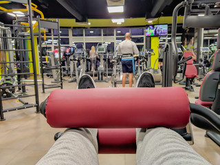 First person view of leg day exercise for heavy weight lifting and body building in a well equipped and modern gym interior with other people working out
