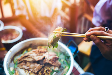 People cooking meat and grill. Food are vegeteble. People use chopsticks.