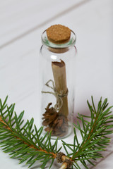 Note in a glass bottle. Stands on white painted wooden boards. Near the fir branches.