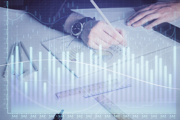 Double exposure of man's hands writing notes of stock market with forex chart.