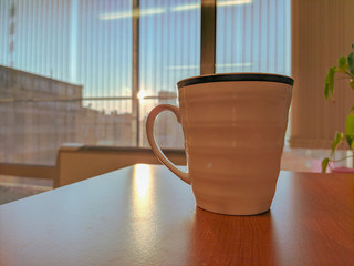 Drinking coffee or tea during work from a white plain mug cup placed on a desk with a beautiful sunny background