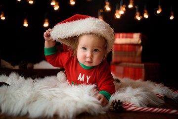 7 month old girl in a red Christmas costume on a background of retro garlands sits on a fur