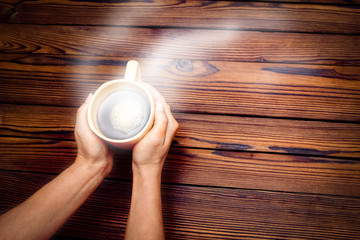 Female hands holding cup of coffee on wooden background