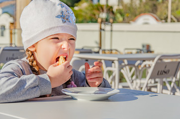 Hungry little girl eating cake in cafe outside