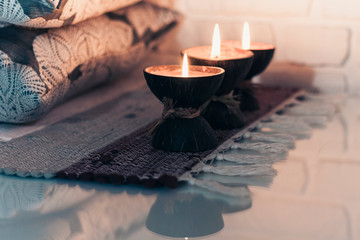 Burning spa aroma candle in coconut shell on a knitted multicolored rug and gray pillows opposite...