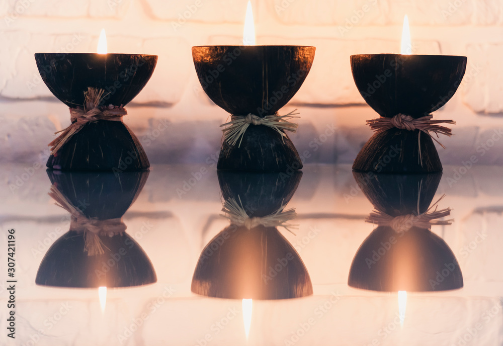 Wall mural Burning spa aroma candles in coconut shell on a glass white table, cozy home interior.