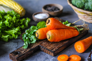 Photo of Fresh Carrots On Wooden Cutting Board. On wooden Dark Background. Slice of carrots with green leaves. Carrot around vegetables, salt, black pepper, corn, broccoli. Drops of water. Image