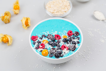 Fototapeta na wymiar Breakfast smoothie bowl with blue spirulina, yogurt, raspberries, blueberries, Blackberries, physalis and coconut flakes. Detox smoothie bowl. Vegan food.