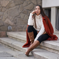 Lifestyle portrait of a stylish beautiful girl sitting on a stairs in colorful clothes. Outdoor shot of people emotions.