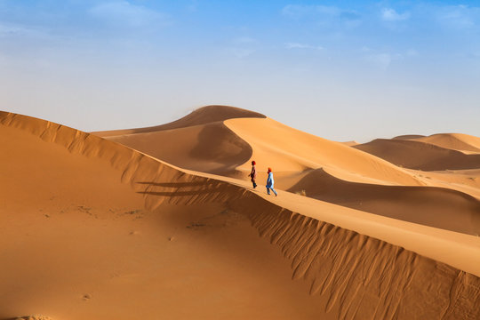 Two Bedouin young men walk across the dunes