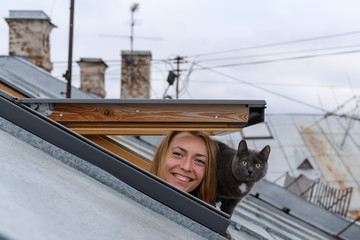 Young woman with cat looking from roof window 