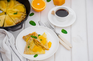 Crepe suzette with orange sauce and a cup of coffee on a white wooden background. Tasty and fragrant breakfast.