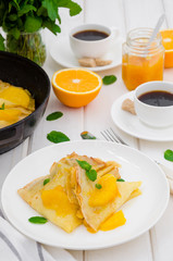 Crepe suzette with orange sauce and a cup of coffee on a white wooden background. Tasty and fragrant breakfast.