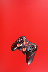 A black joystick game controller hovers isolated on a red background. Interactive entertainment © Alexander