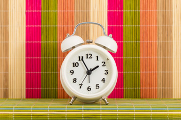 White alarm clock is over multicolor bamboo mat background