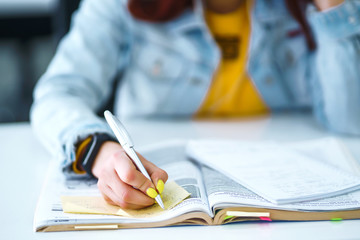 Young woman's hands holding pen and writing in daily planner. Teenager student in a yellow sweater prepares for exams. Freelancer works and makes notes. Startup small business.
