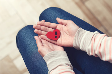 Red heart symbol with man's black boot print is in woman's hands