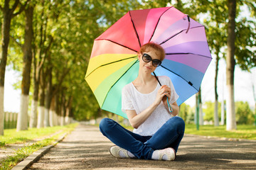 Happy blond girl holding colorful rainbow umbrella in hands