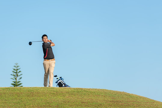 Professional golfer asian man approach on the tee off for swing and hitting golf ball and looking fairway in course. Hobby in holiday and vacations in sunny morning on club golf.  Lifestyle sport 