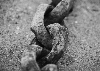 Horizontal close-up image of an old rusted chain used in boat anchors lying on concrete pier in black and white with shallow Depth of Field in Riga, Latvia.