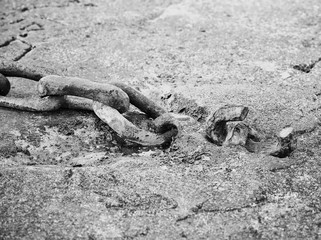 Horizontal close-up image of an old rusted chain used in boat anchors lying on concrete pier in black and white with shallow Depth of Field
