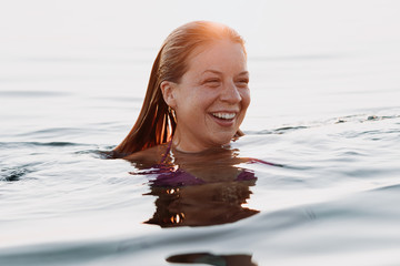 Young happy woman floating in the sea in sunset