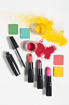 A collection of beautiful red lipsticks, mascara eye shadow and yellow and pink make up powder isolated on a white background shot from above. Powder smeared in a creative way.