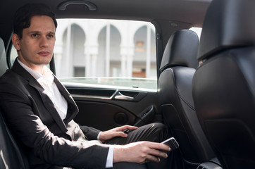 Adult Caucasian male sitting inside car while holding mobile phone.