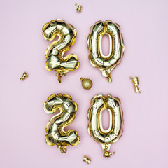 Happy New year 2020 celebration. Gold foil balloons numeral 2020 and golden stars on pastel pink background. Holiday party card or invitation.