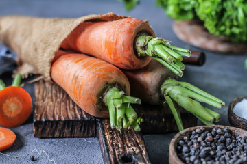 Photo of Fresh Carrots On Wooden Cutting Board. On wooden Dark Background. Slice of carrots with green leaves. Carrot around vegetables, salt, black pepper, corn, broccoli. Drops of water. Image