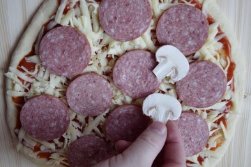 Pizza with cheese, sausage and mushrooms. A man's hand. The process of cooking Italian pizza.
