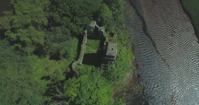 Rising aerial tilting down over the ancient ruins of Loch Dochart Castle on an island in the middle of the loch in the Scottish Highlands showing grass inside, reclaimed by nature