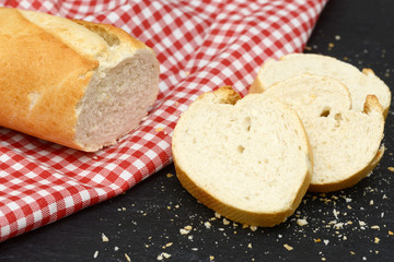 rustic crusty white bread lying on black slate on red white towel in the kitchen