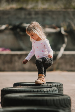 Happy joyful little girl having fun and walking through row of black car tires while playing outdoors on summer day