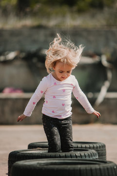 Happy joyful little girl having fun and jumping in row of black car tires while playing outdoors on summer day