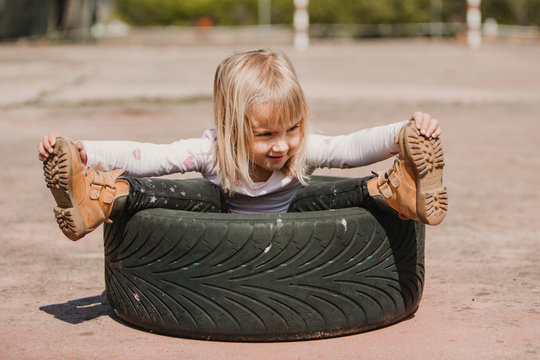 Happy adorable little girl sitting inside car tire while having fun and playing outdoors on summer day