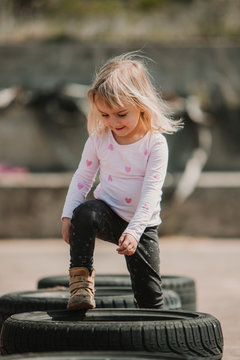Happy joyful little girl having fun and walking through row of black car tires while playing outdoors on summer day