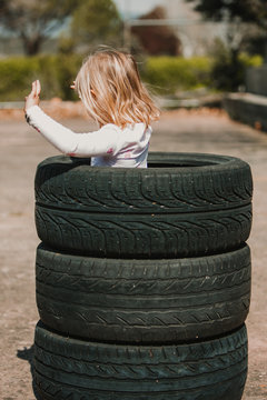 From Behind anonymous of little girl standing in stack of car tires while having fun and playing outdoors on summer day
