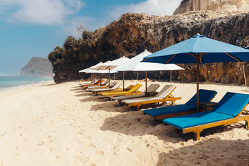 Fototapeta na wymiar Wooden deck chairs with umbrellas along the coastline. Melasti Beach in the Indian Ocean. Indonesia, Bali.