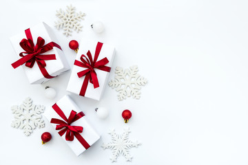 Fototapeta premium Gift boxes wrapped white paper and red ribbon decorated baubles and snowflakes on white background. Top view. Flat lay. Christmas and New Year