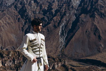 noise effect, selective focus: stylish Georgian man dressed in white national men's suit. Portrait of Georgian groom during wedding on Caucasus mountains