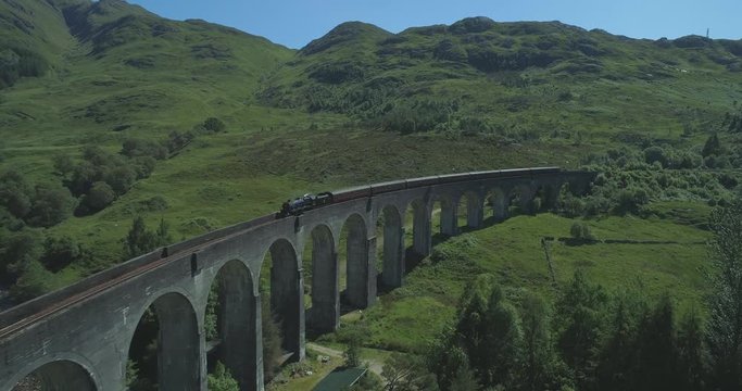 Wide aerial of the Hogwart's Express (Harry Potter) steam train travelling over the Glen Finnan Viaduct in the Scottish Highlands on a sunny day