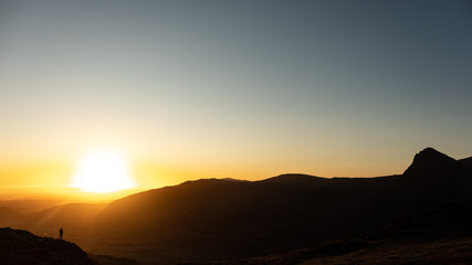 A hiker silhouetted against beautiful orange sunrise in mountains