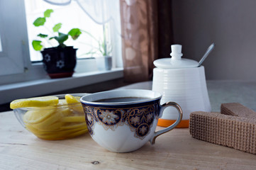 Cup, lemons, sugar bowl, waffles on a wooden table near the window