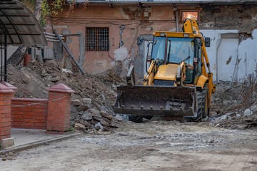 Fototapeta na wymiar A large yellow excavator stands among the ruins of an old house
